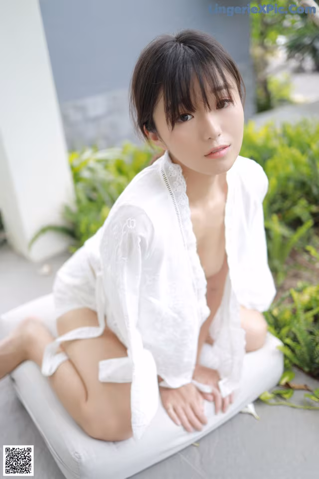 A woman in a white robe sitting on a white cushion.