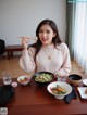 A woman sitting at a table with bowls of food and chopsticks.