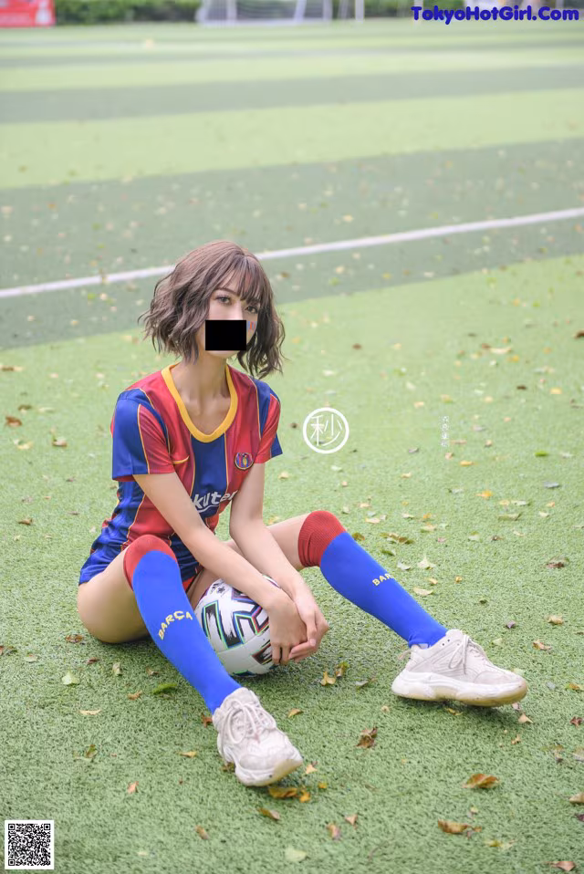 A woman sitting on the ground with a soccer ball.