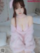 A woman in a pink bunny costume sitting on a bed.