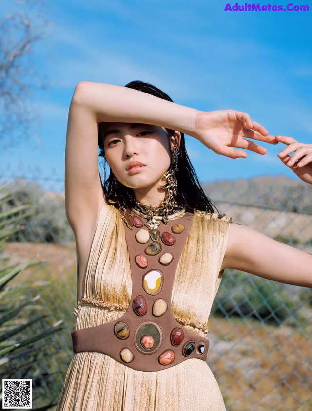 A woman in a gold dress standing in front of a fence.