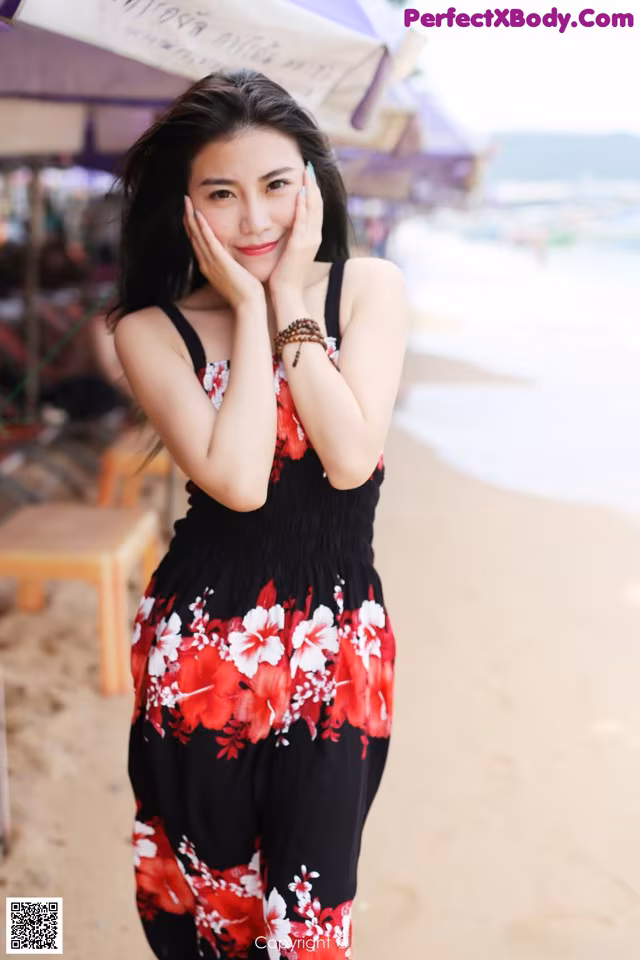 A woman in a black and red floral dress on the beach.