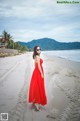 A woman in a red dress walking on the beach.