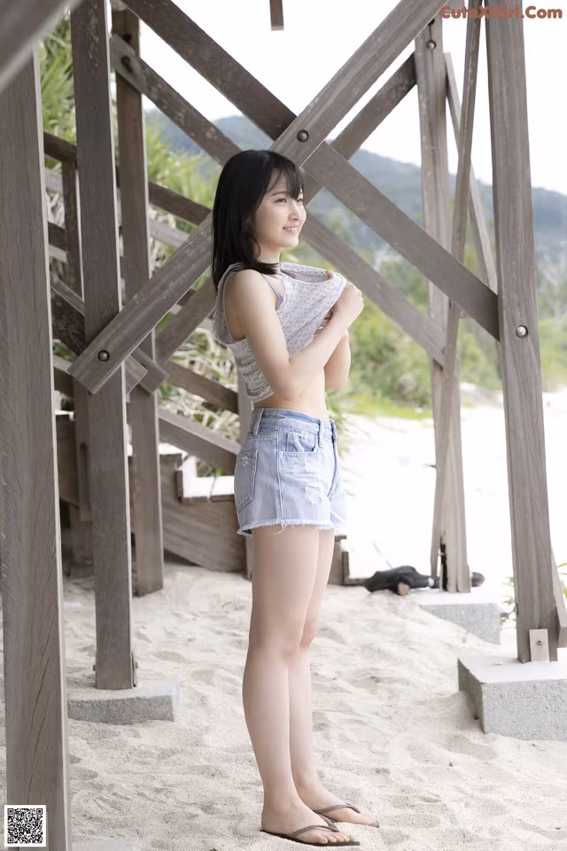 A woman standing on a sandy beach next to a wooden structure.