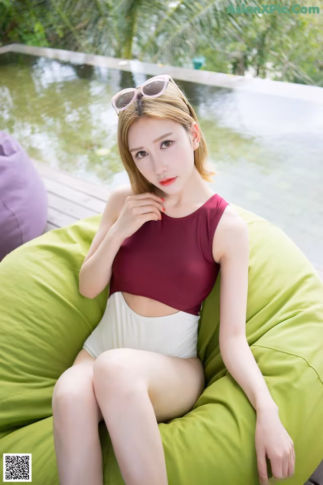 A woman sitting on a green bean bag chair next to a pool.