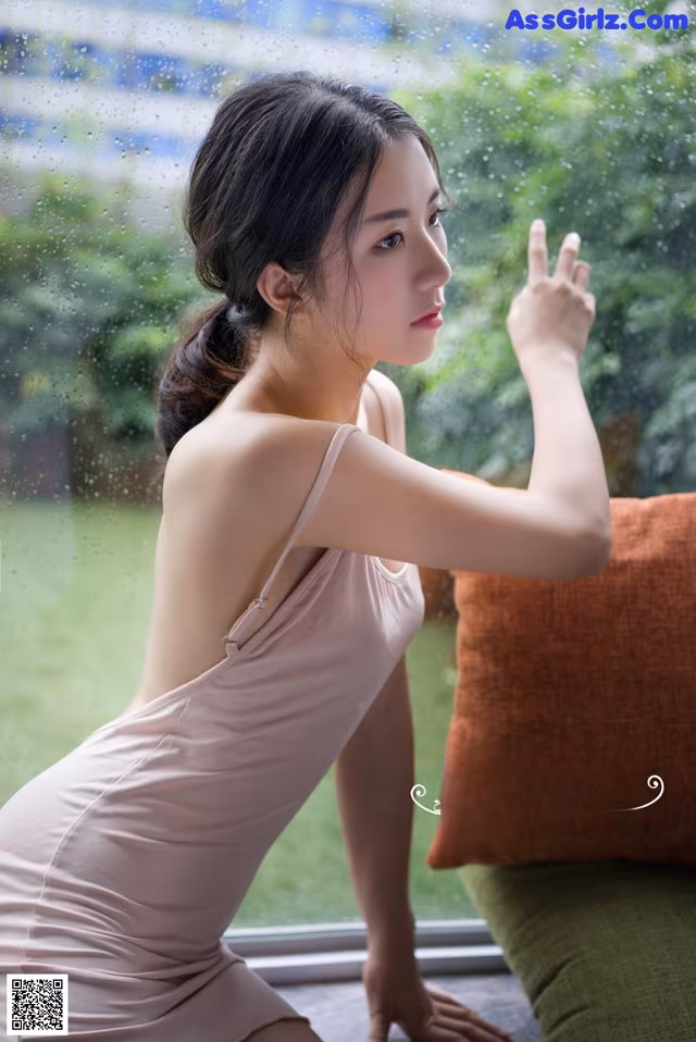 A woman in a pink dress sitting on a window sill.