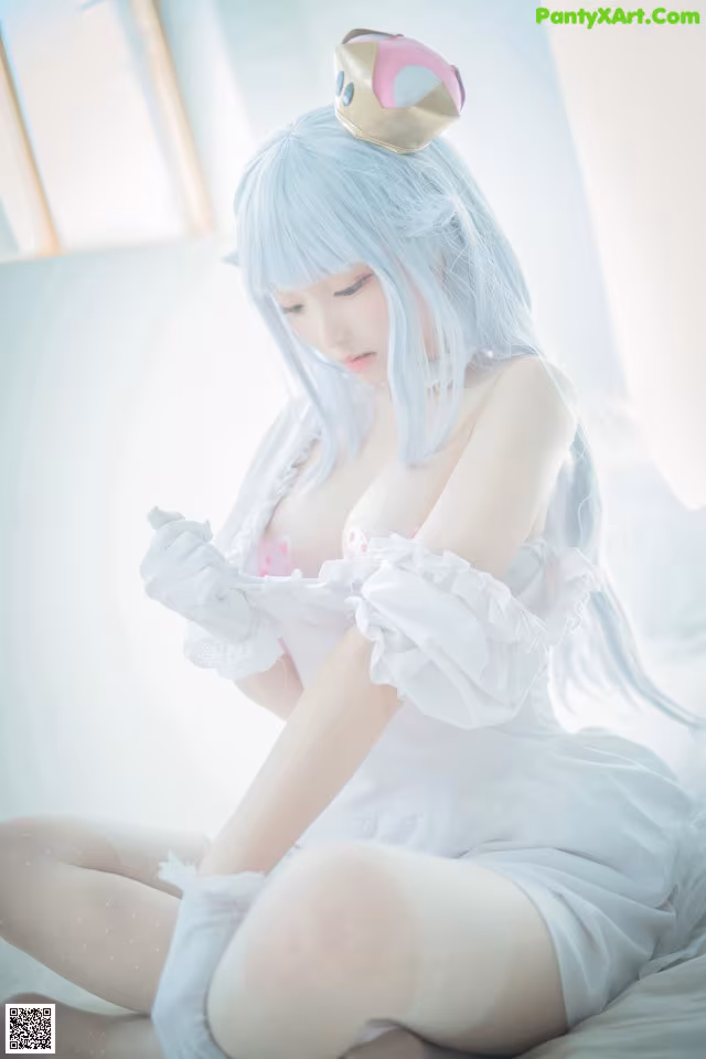 A woman in a white dress sitting on a bed.