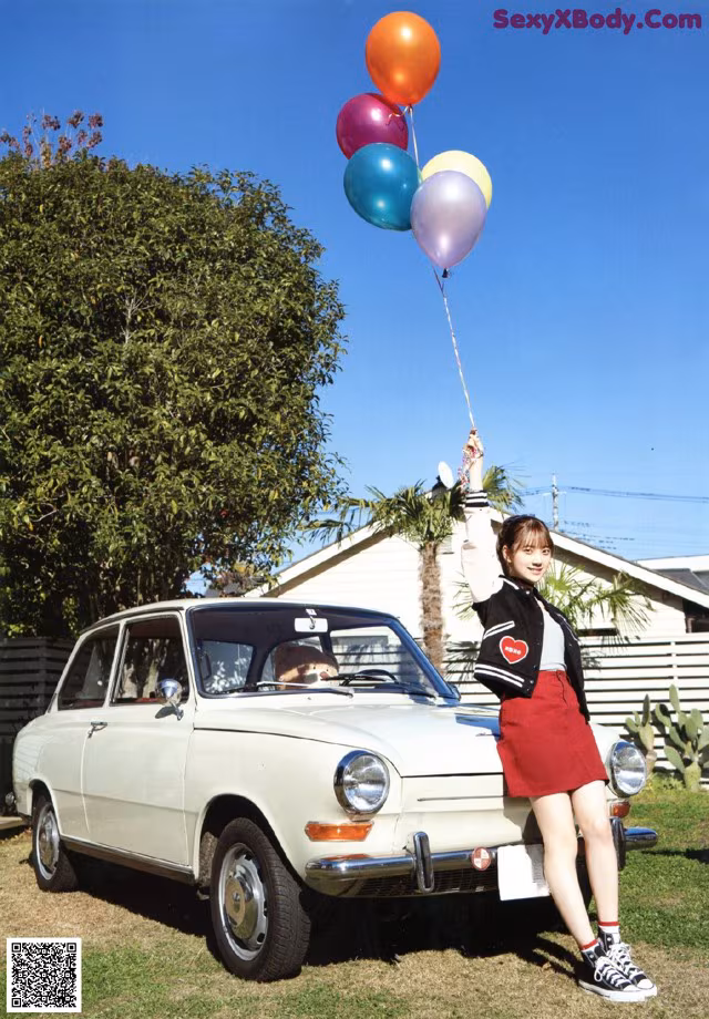 A woman holding a bunch of balloons in front of a car.