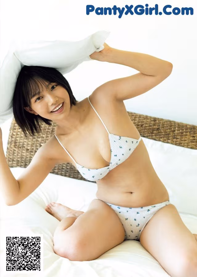 A woman in a white bikini sitting on a bed.