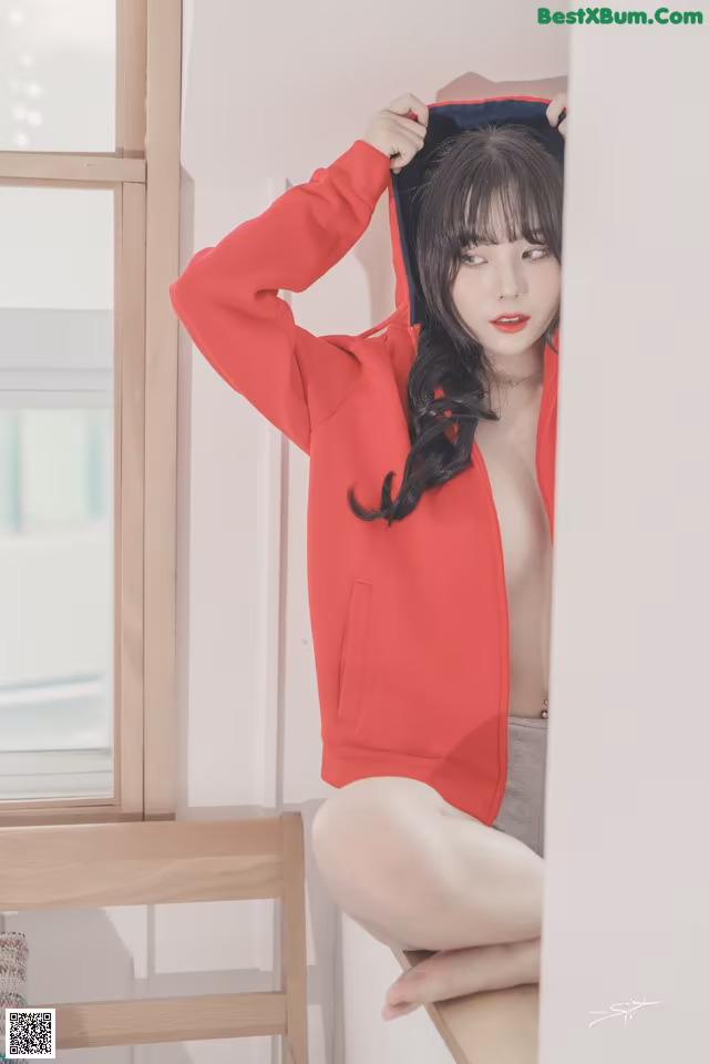 A woman in a red hoodie sitting on a window sill.