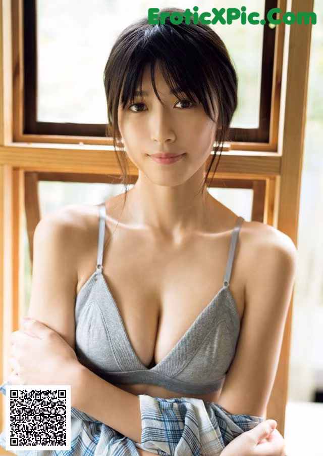 A woman in a gray bra top is posing by a window.