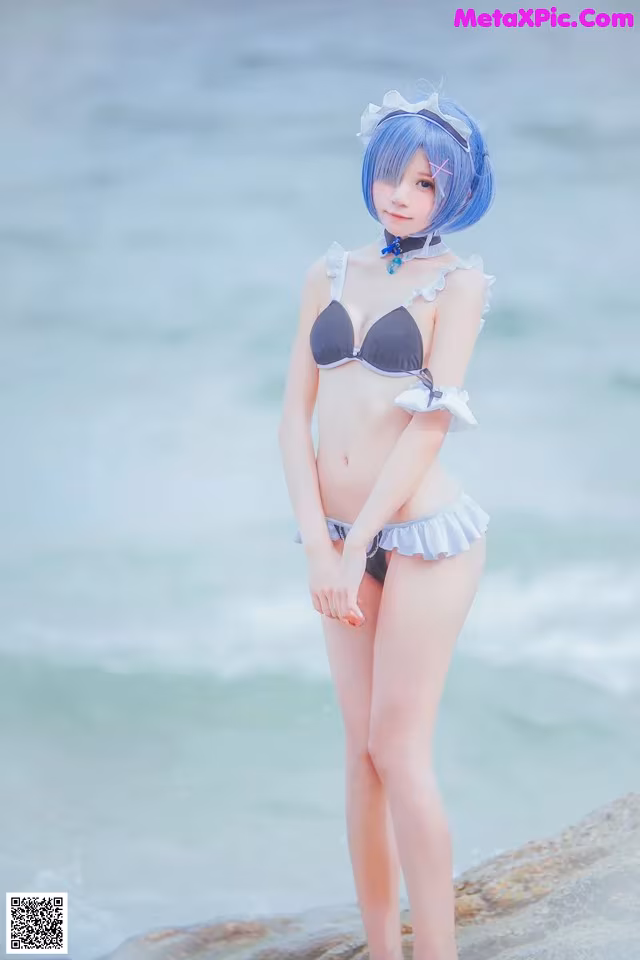 A woman in a bikini standing on a rock by the ocean.