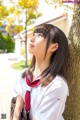 A woman in a school uniform leaning against a tree.