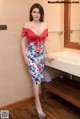 A woman in a red top and blue skirt posing in a bathroom.