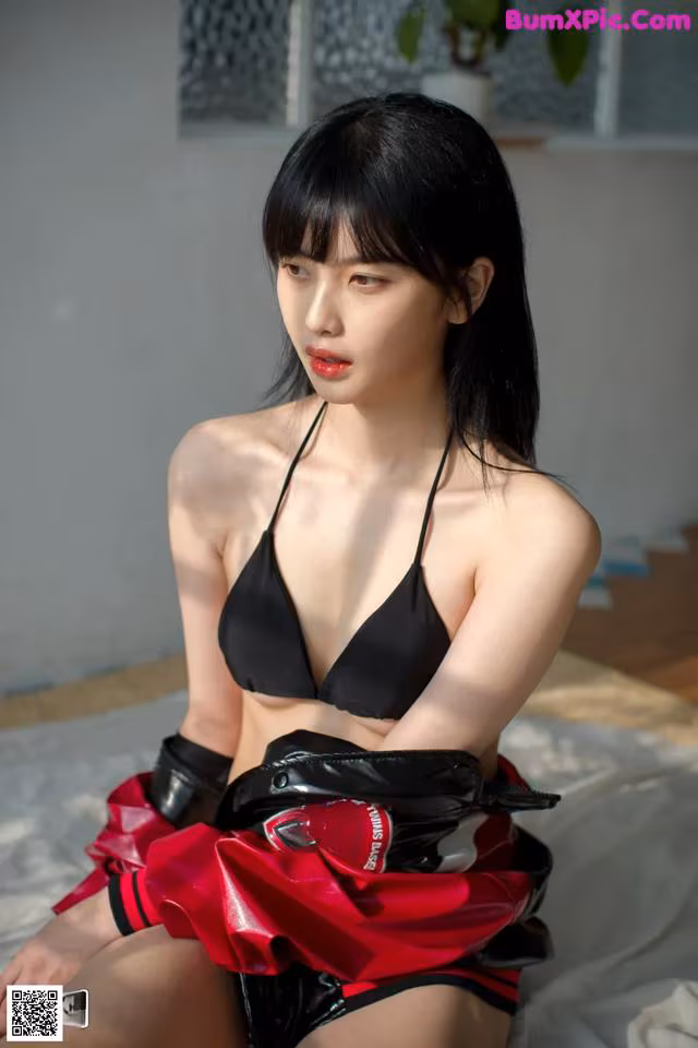 A woman in a black bikini sitting on a bed.