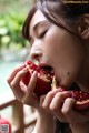 A woman eating a pomegranate with her eyes closed.