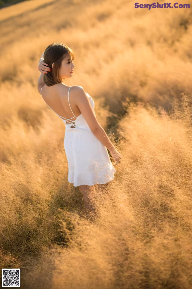 A woman in a white dress standing in a field of tall grass.