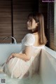 A woman sitting in a bathtub in a white dress.