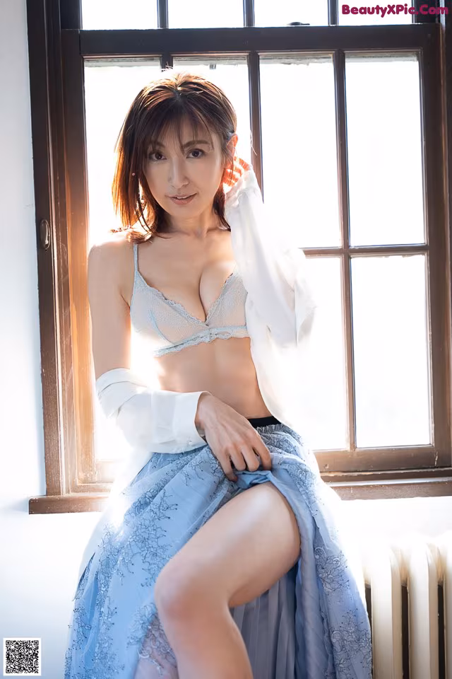 A woman sitting on a window sill in a blue skirt.