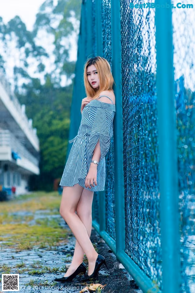 A woman leaning against a fence in a striped dress.