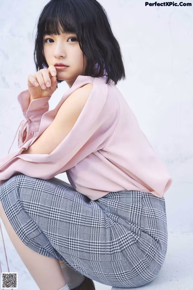 A woman sitting on the ground wearing a pink shirt and plaid pants.