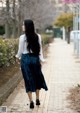 A woman walking down a sidewalk in a blue skirt.